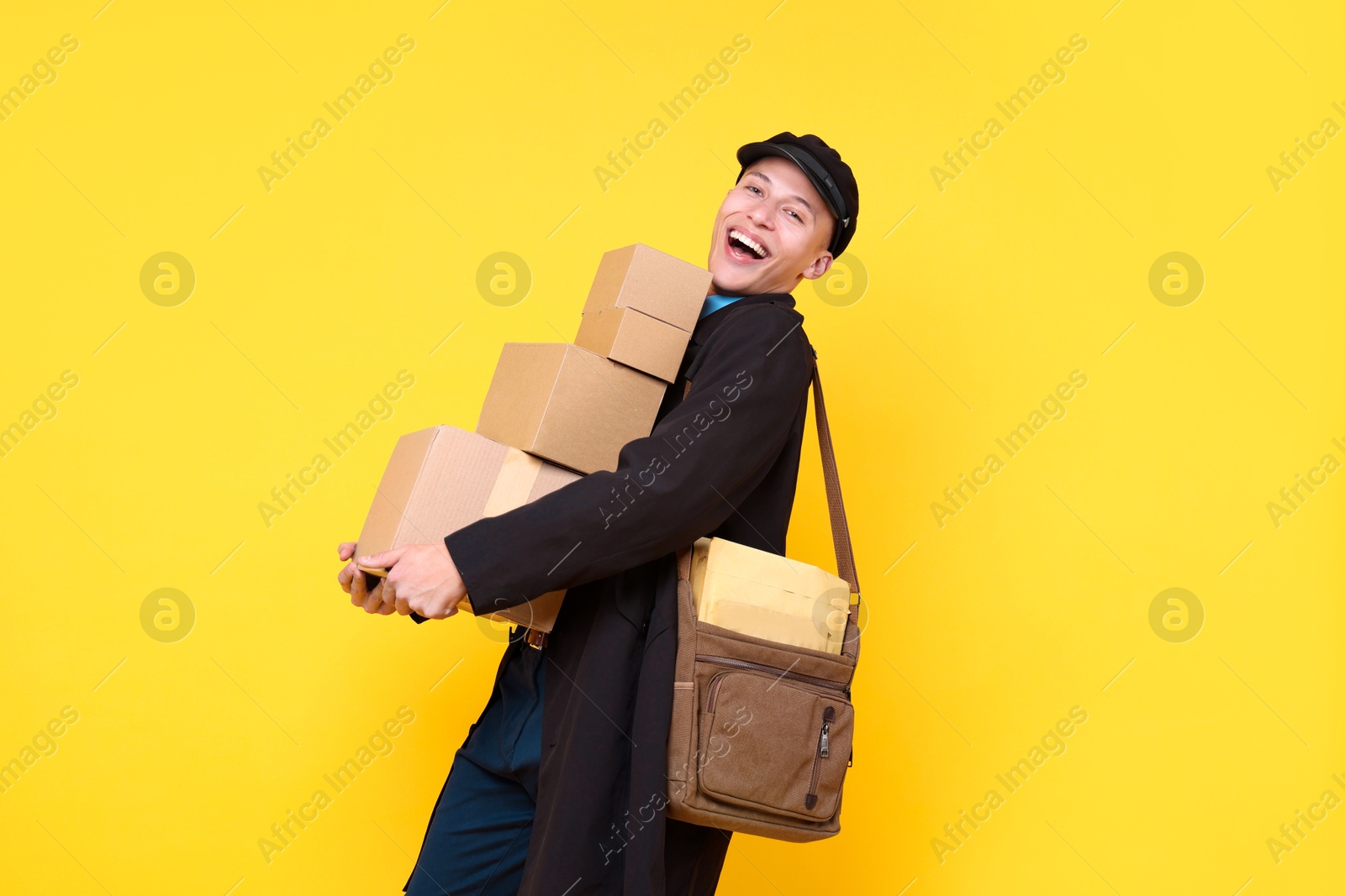 Photo of Happy postman with bag and parcels on yellow background