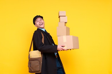 Photo of Happy postman with bag and parcels on yellow background