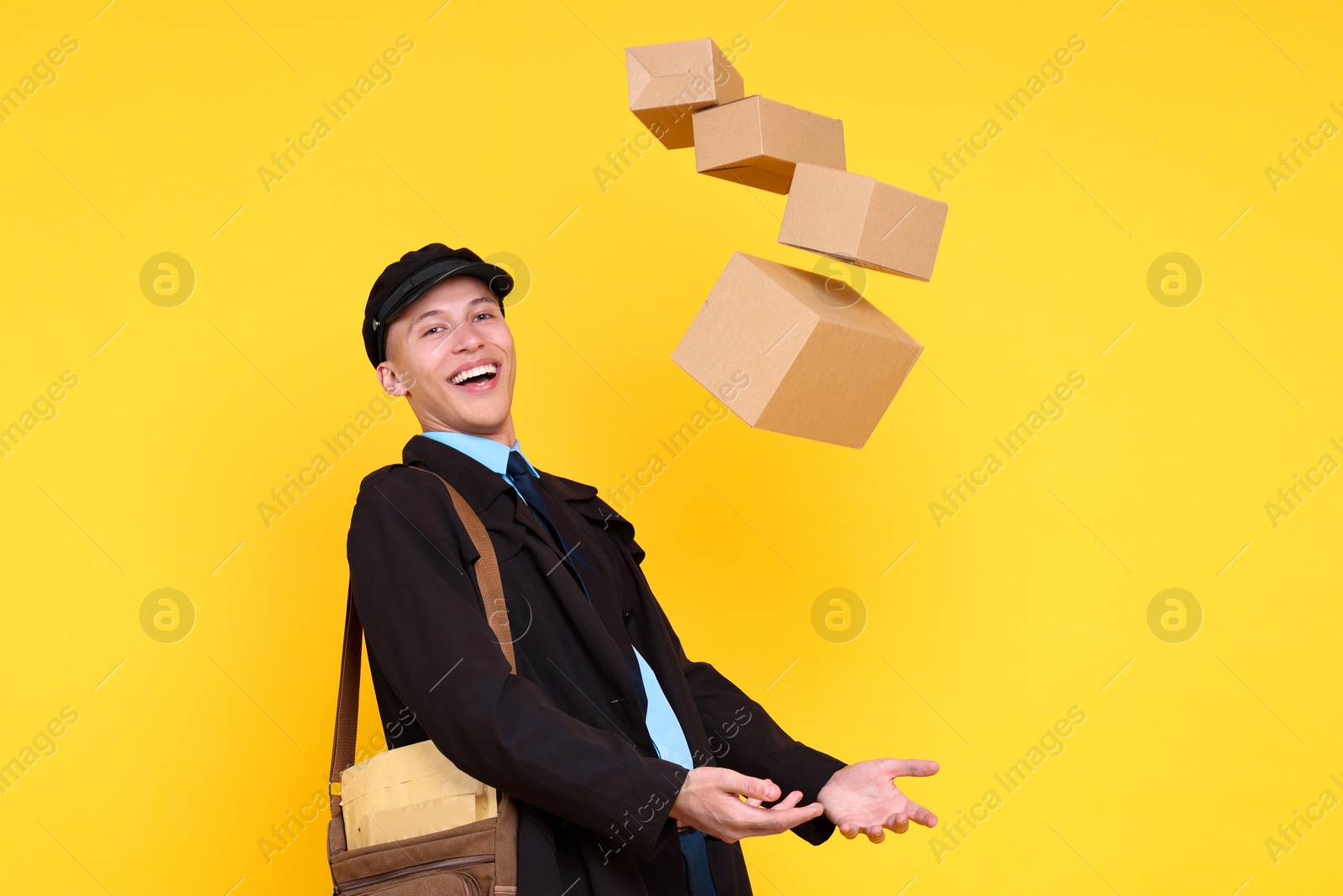 Photo of Happy postman with bag throwing parcels on yellow background