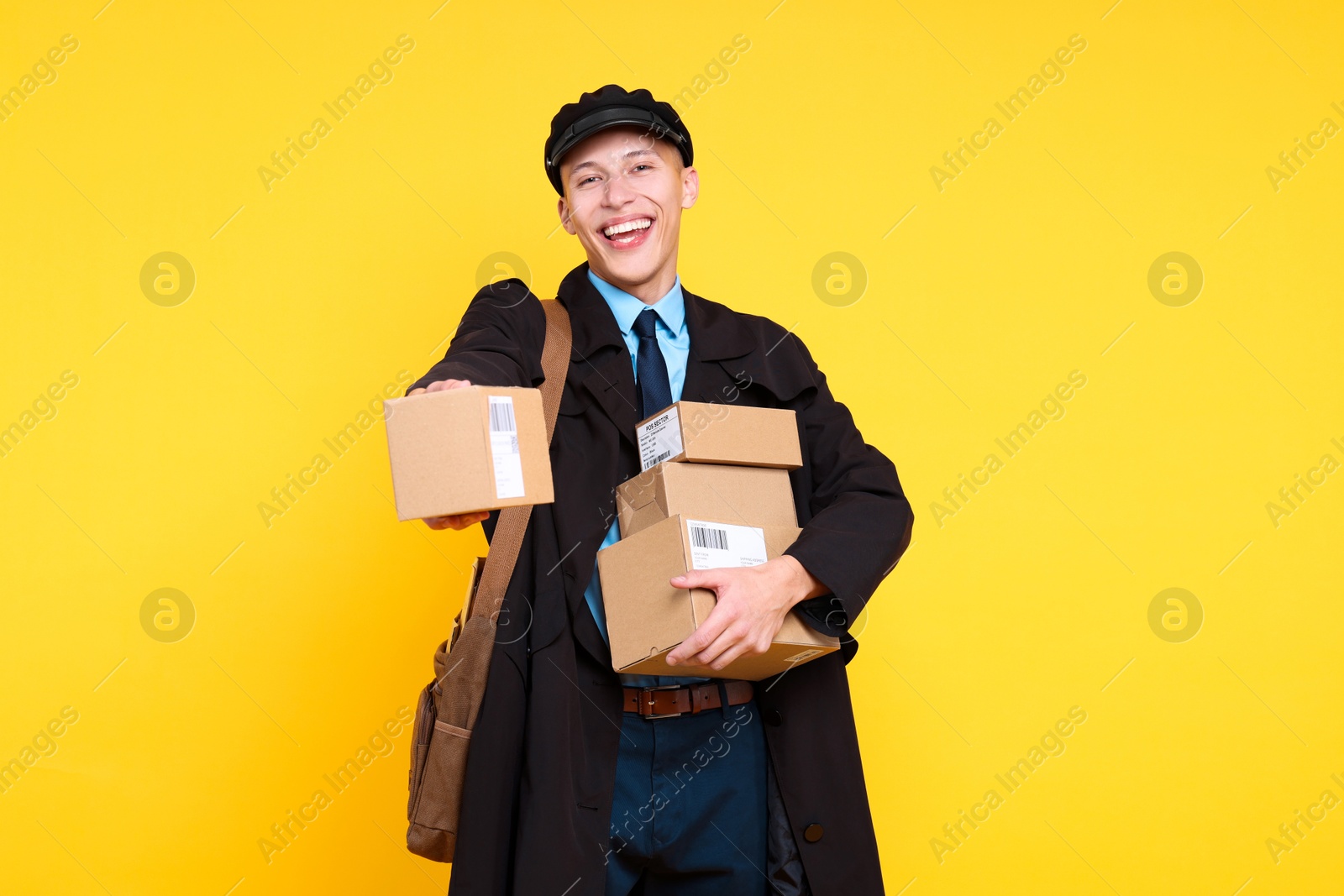 Photo of Happy postman with bag giving parcel on yellow background