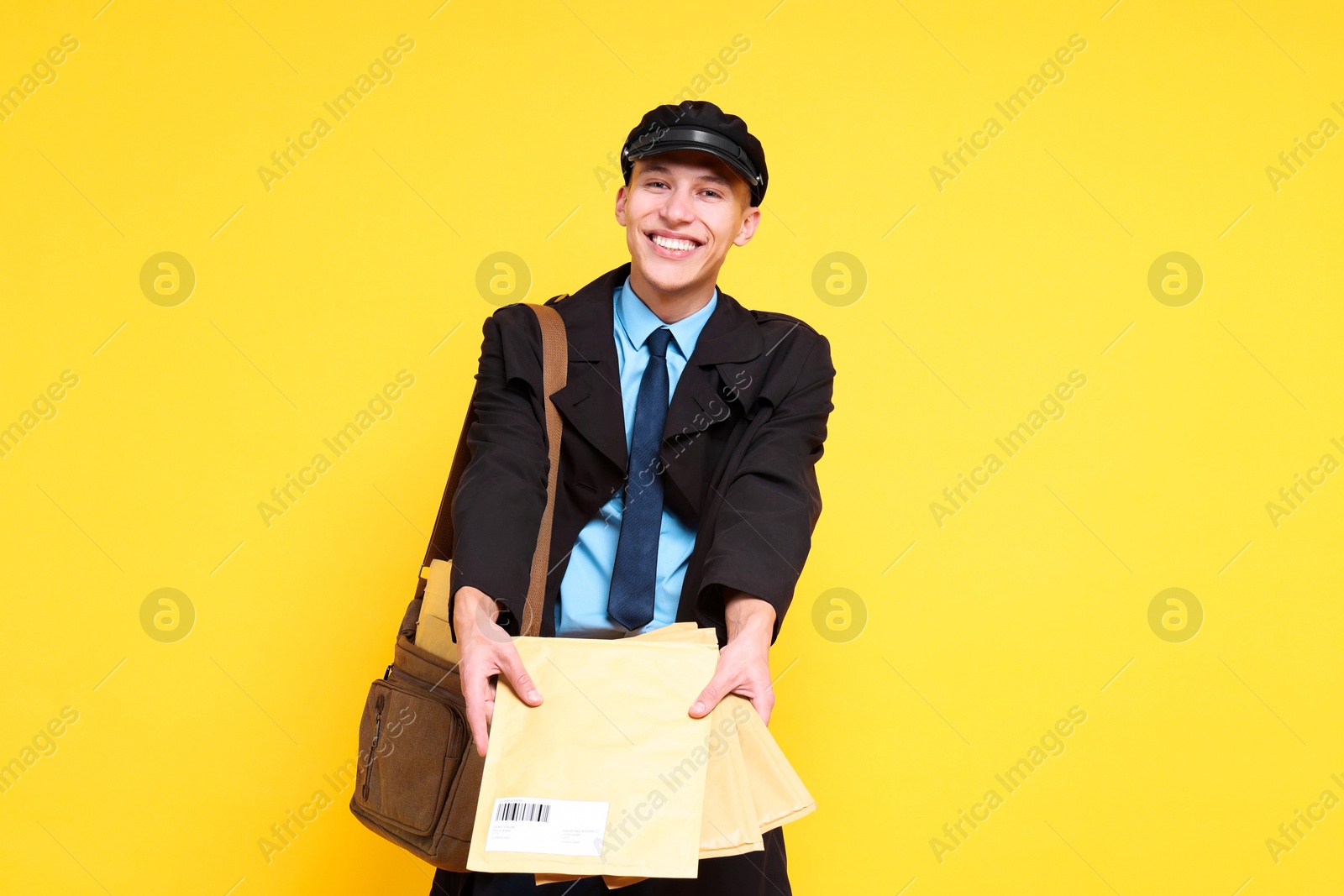 Photo of Happy postman with bag and envelopes on yellow background