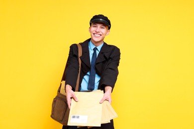 Photo of Happy postman with bag and envelopes on yellow background