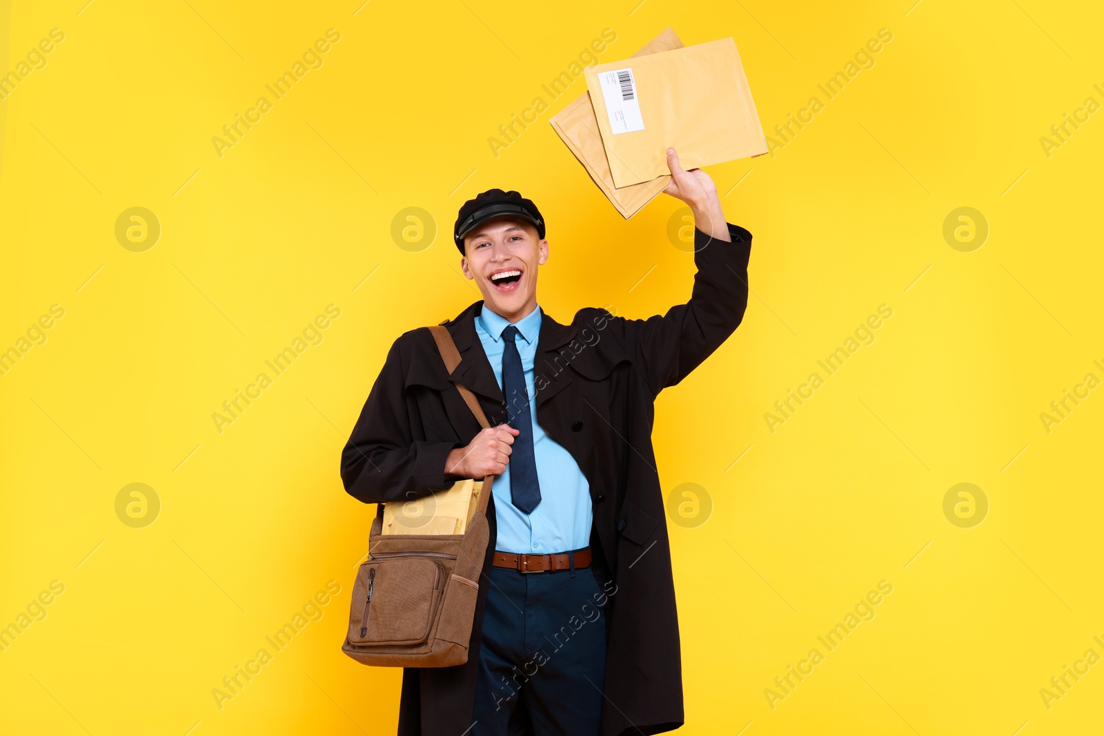 Photo of Happy postman with bag and envelopes on yellow background