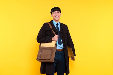 Photo of Happy postman with bag and envelopes on yellow background