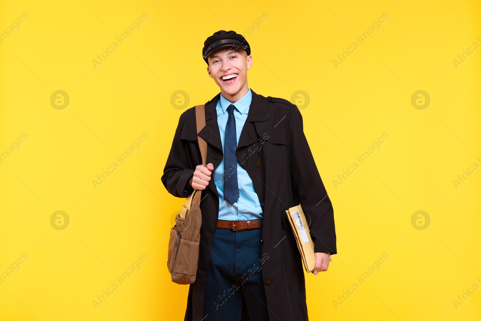 Photo of Happy postman with bag and envelopes on yellow background