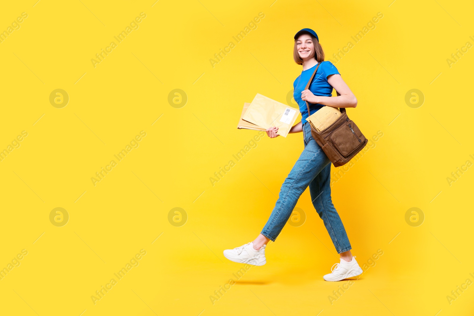 Photo of Happy postwoman with bag and envelopes on yellow background. Space for text