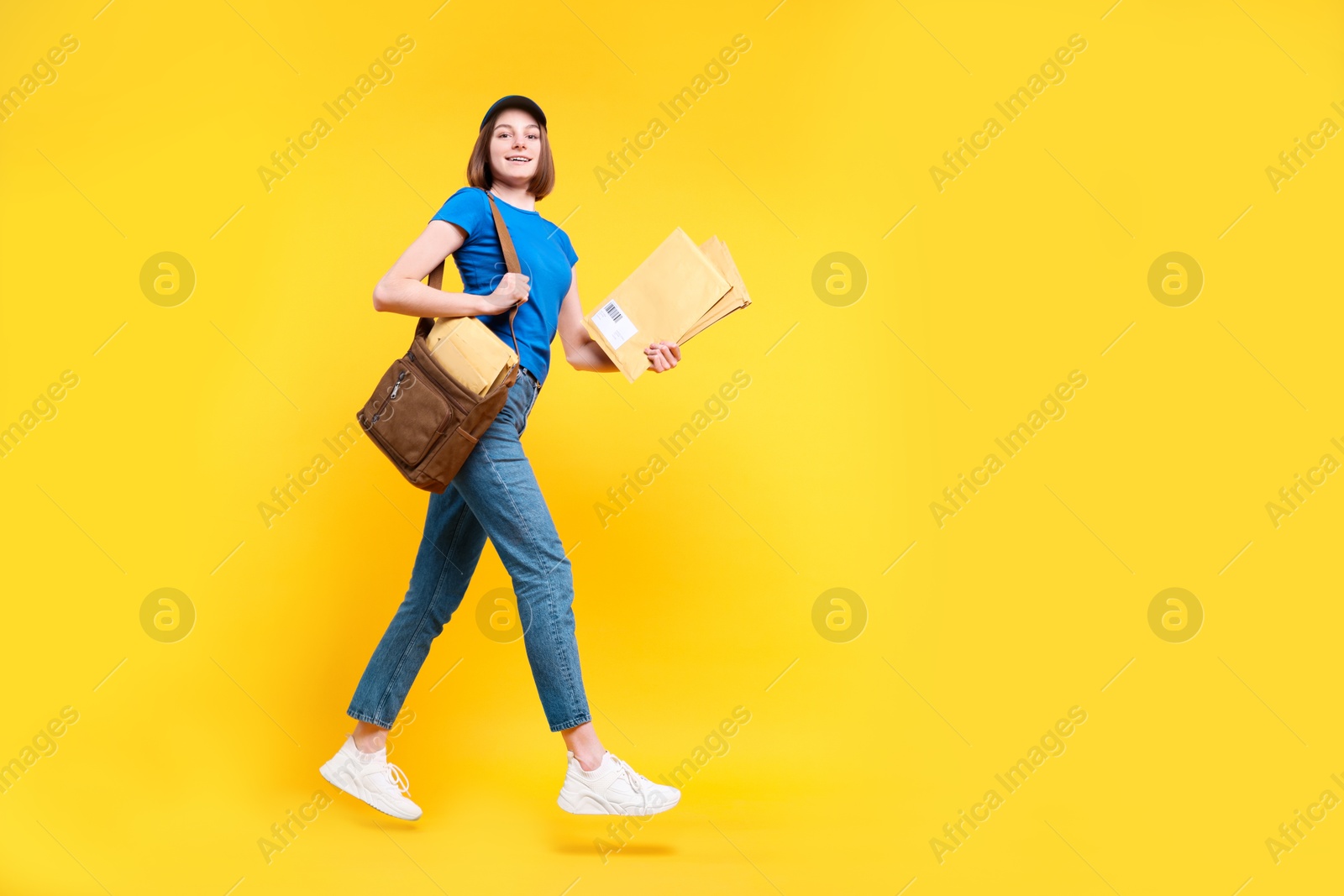 Photo of Happy postwoman with bag and envelopes jumping on yellow background. Space for text