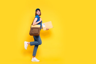 Photo of Happy postwoman with bag and envelopes on yellow background. Space for text