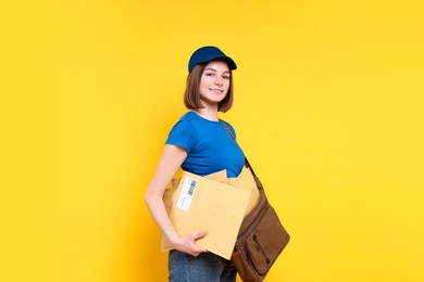 Photo of Happy postwoman with bag and envelopes on yellow background. Space for text