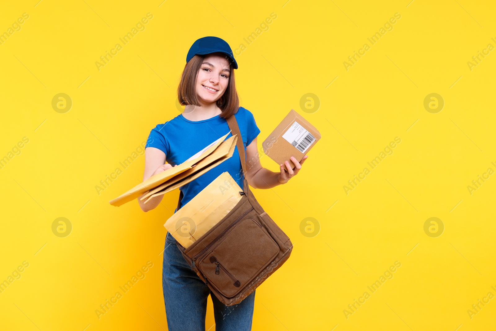 Photo of Happy postwoman with bag and parcel giving envelopes on yellow background