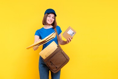 Photo of Happy postwoman with bag and parcel giving envelopes on yellow background