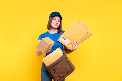 Photo of Happy postwoman with bag and envelopes giving parcel on yellow background