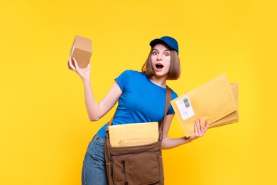 Emotional postwoman with bag, parcel and envelopes on yellow background