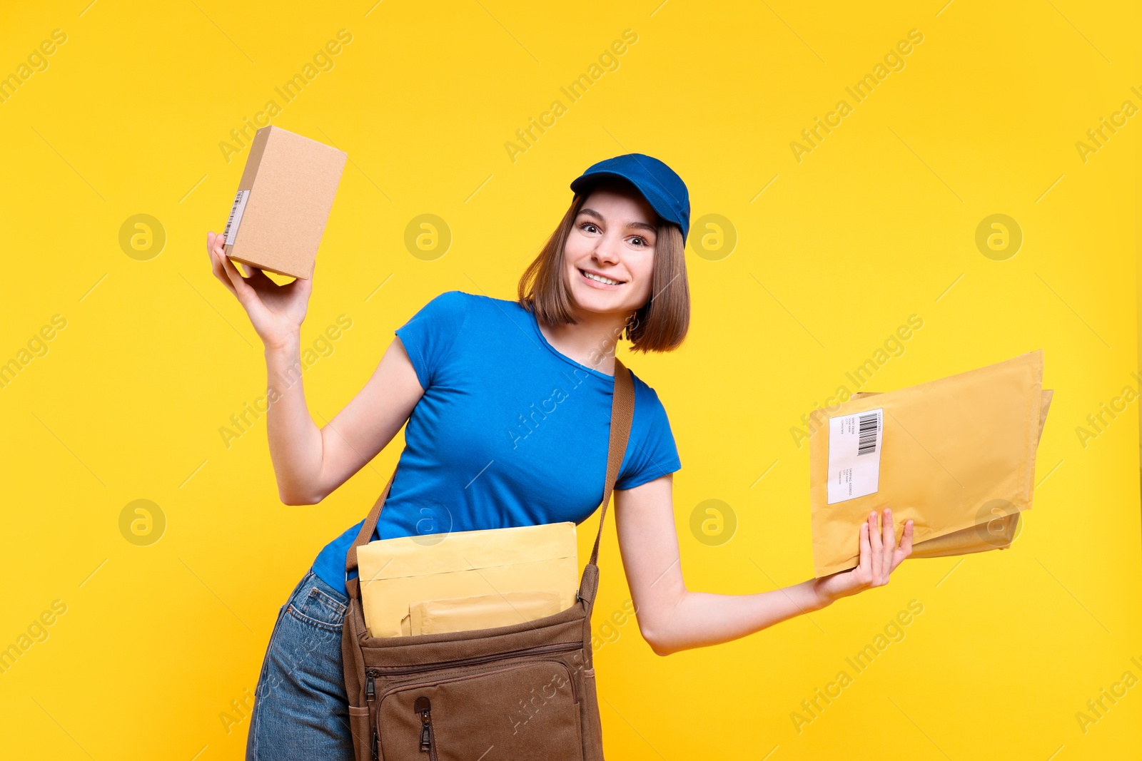 Photo of Happy postwoman with bag, parcel and envelopes on yellow background