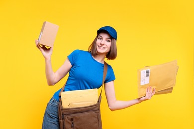 Photo of Happy postwoman with bag, parcel and envelopes on yellow background