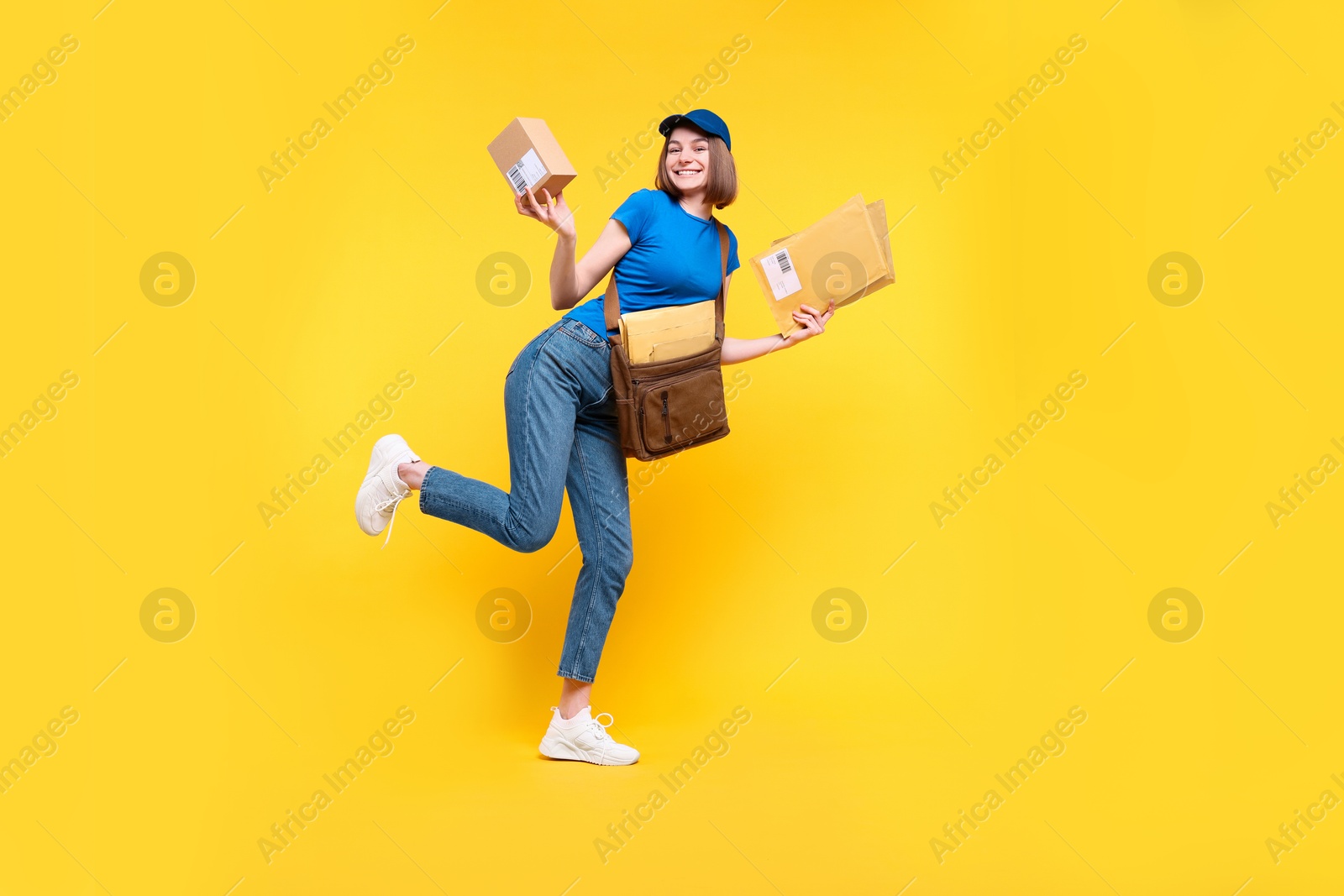 Photo of Happy postwoman with bag, parcel and envelopes on yellow background. Space for text