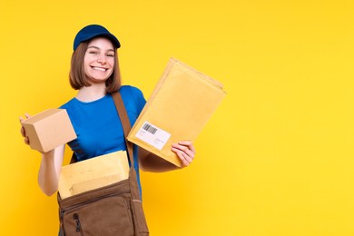 Photo of Happy postwoman with bag, parcel and envelopes on yellow background. Space for text