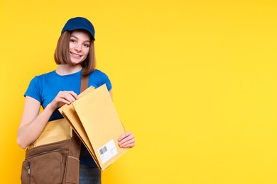 Photo of Happy postwoman with bag and envelopes on yellow background. Space for text