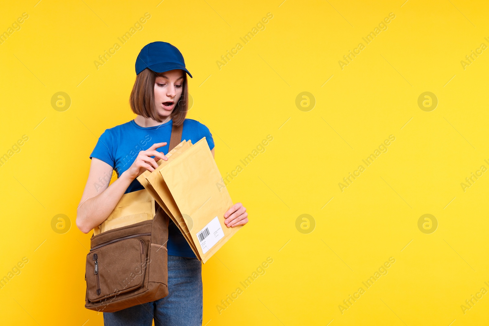 Photo of Surprised postwoman with bag and envelopes on yellow background. Space for text