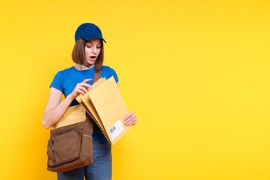 Photo of Surprised postwoman with bag and envelopes on yellow background. Space for text