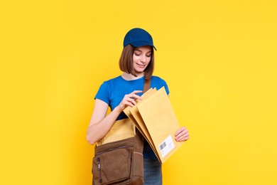 Photo of Happy postwoman with bag and envelopes on yellow background. Space for text