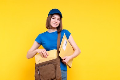 Photo of Happy postwoman with bag and envelopes on yellow background