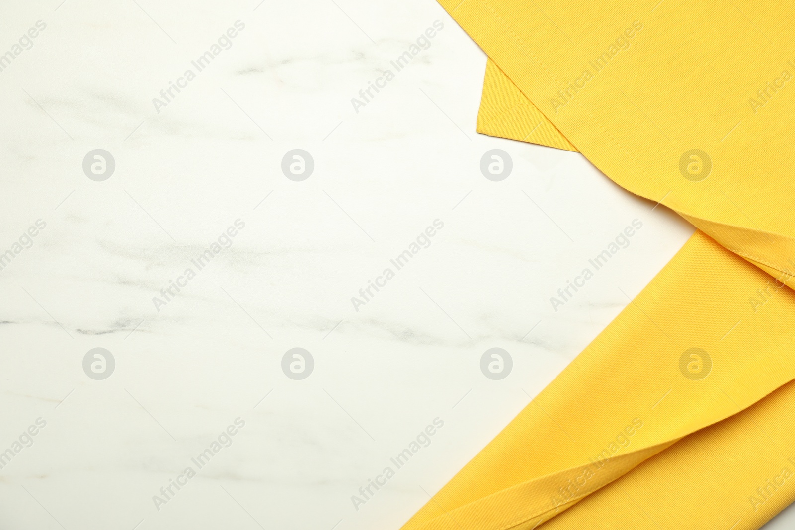 Photo of Yellow tablecloth on white marble background, top view. Space for text