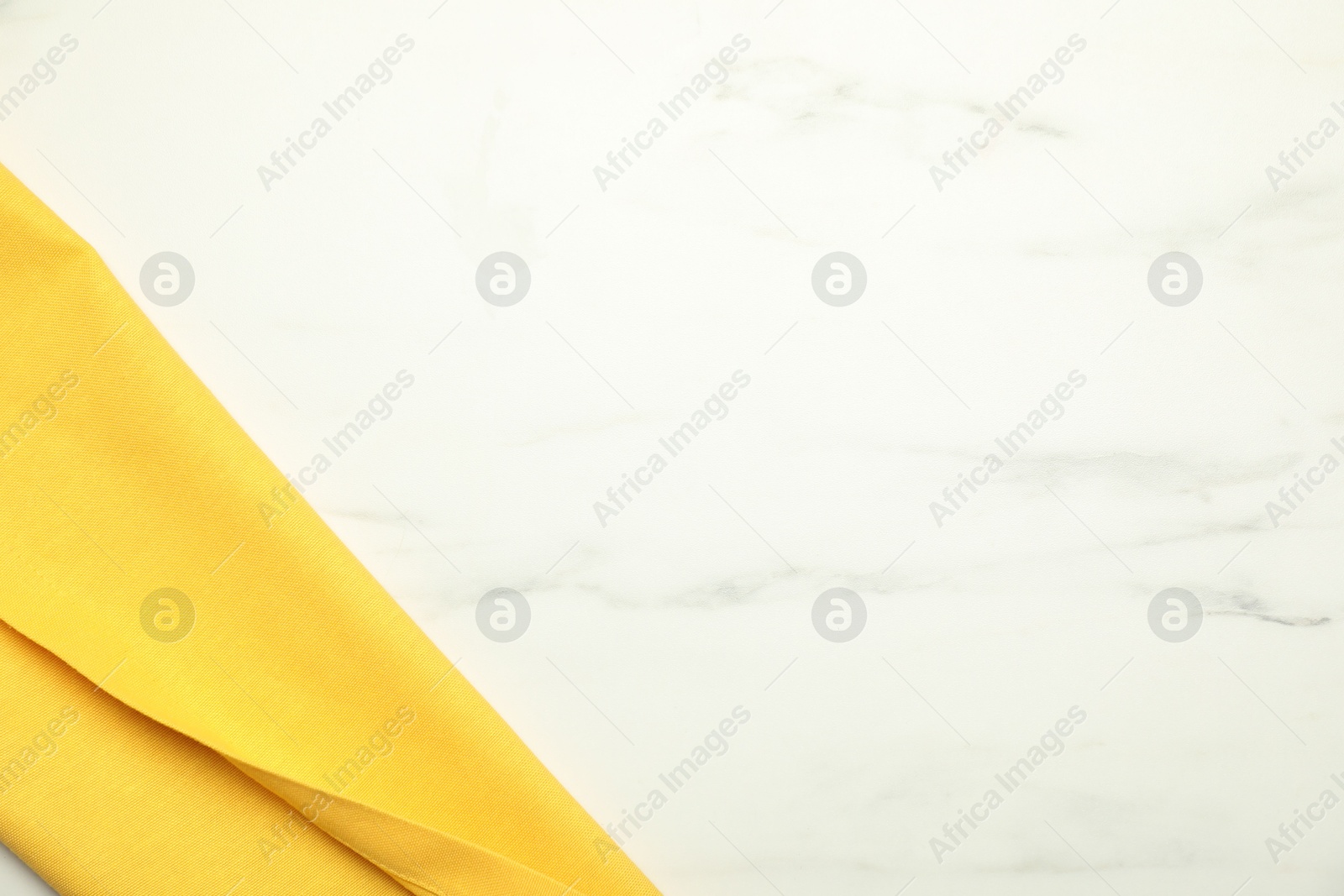 Photo of Yellow tablecloth on white marble background, top view. Space for text