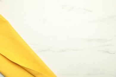 Photo of Yellow tablecloth on white marble background, top view. Space for text