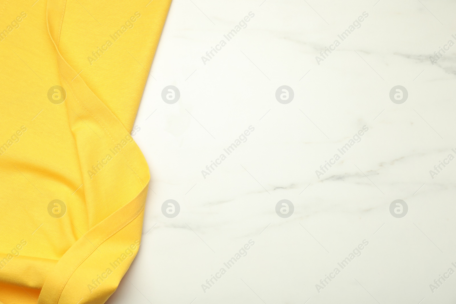 Photo of Yellow tablecloth on white marble background, top view. Space for text