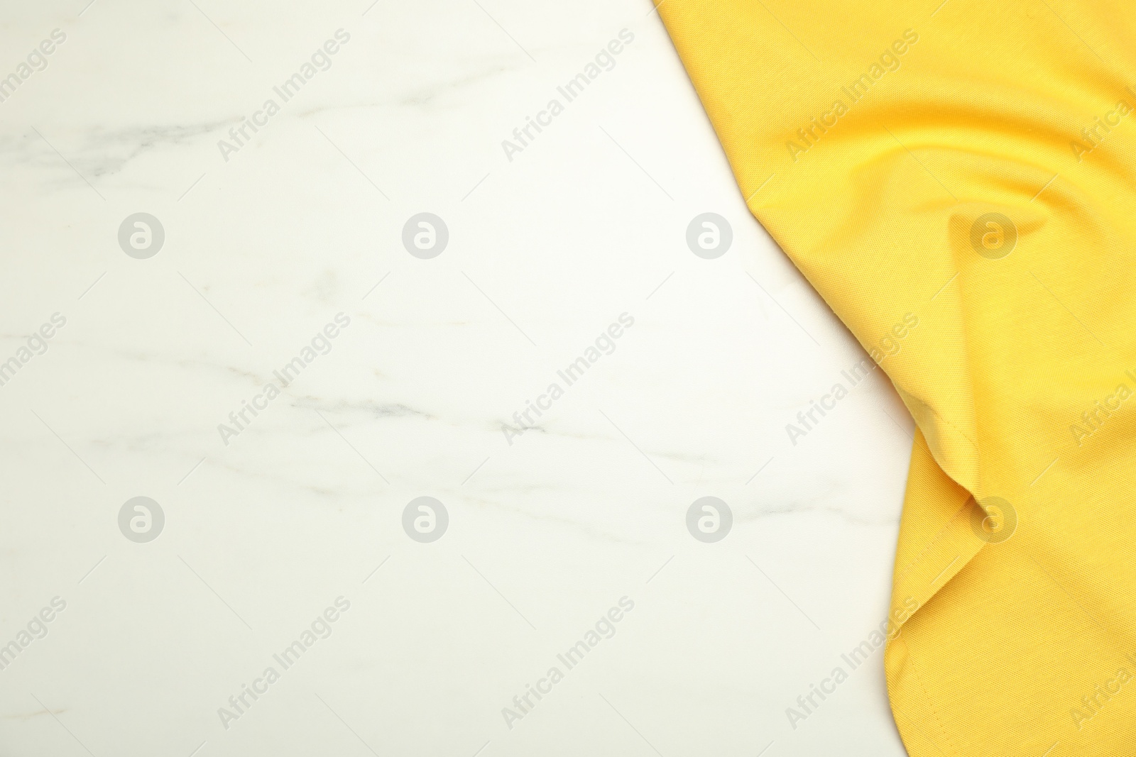 Photo of Yellow tablecloth on white marble background, top view. Space for text