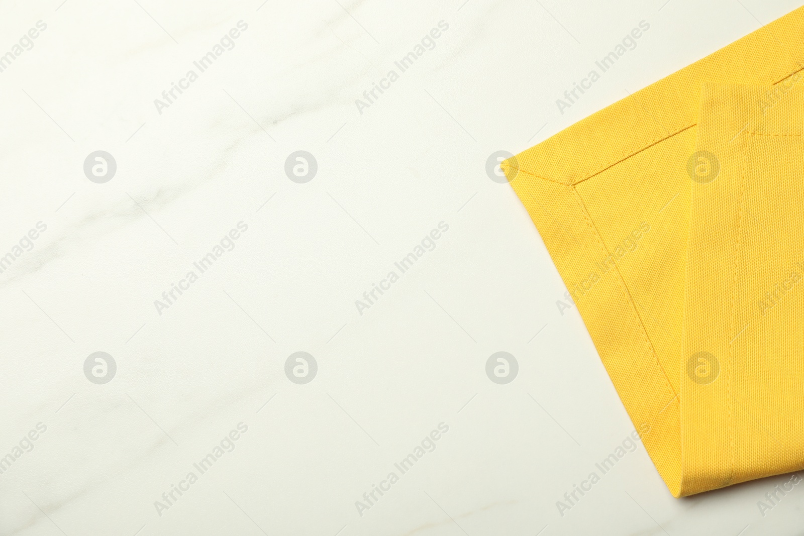 Photo of Yellow tablecloth on white marble background, top view. Space for text