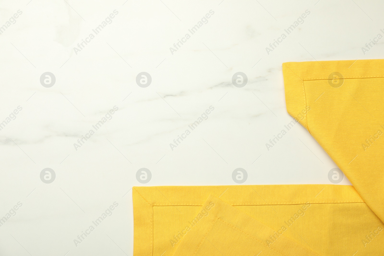 Photo of Yellow tablecloth on white marble background, top view. Space for text