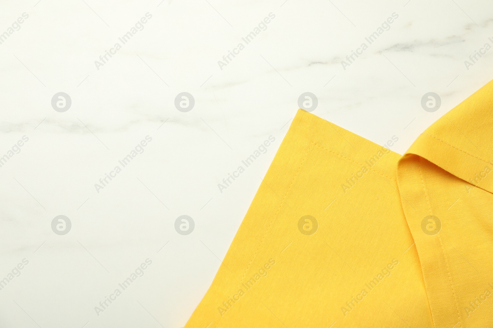 Photo of Yellow tablecloth on white marble background, top view. Space for text