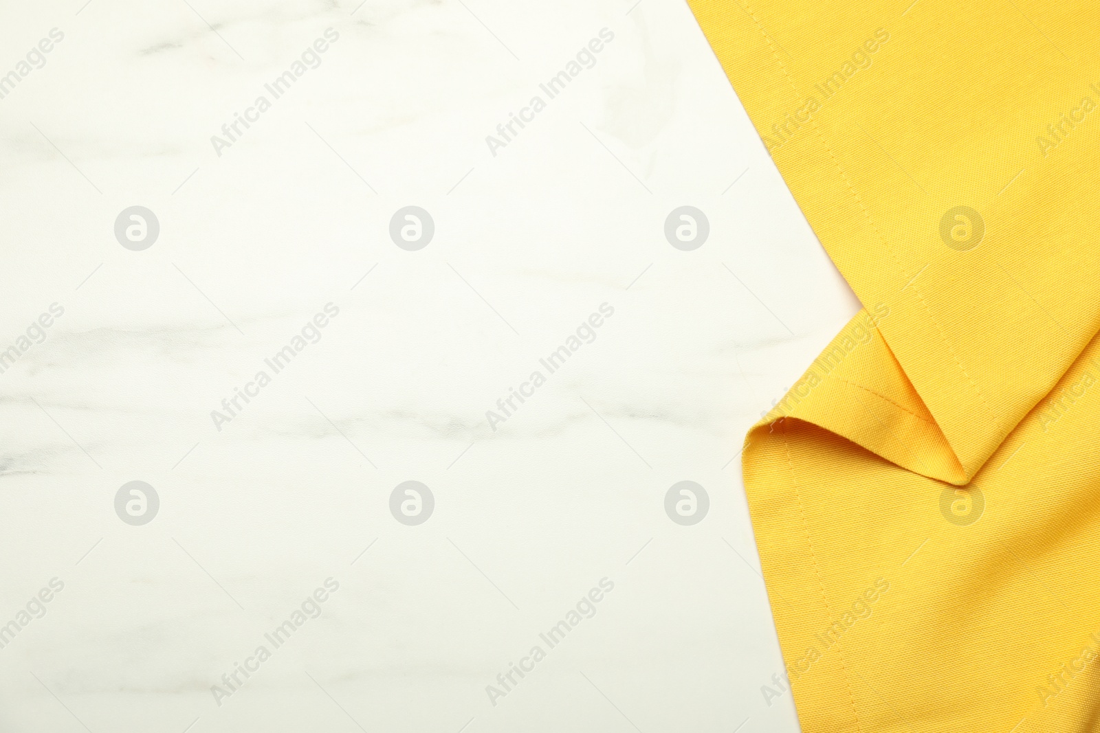 Photo of Yellow tablecloth on white marble background, top view. Space for text