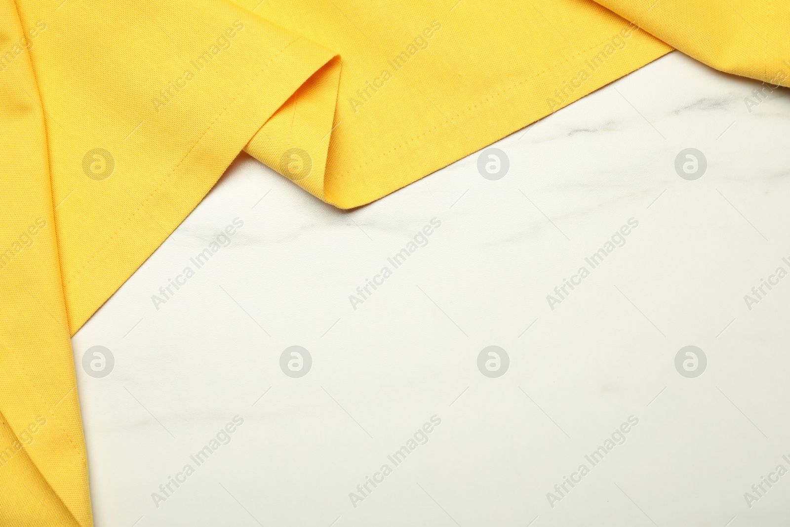 Photo of Yellow tablecloth on white marble background, top view. Space for text