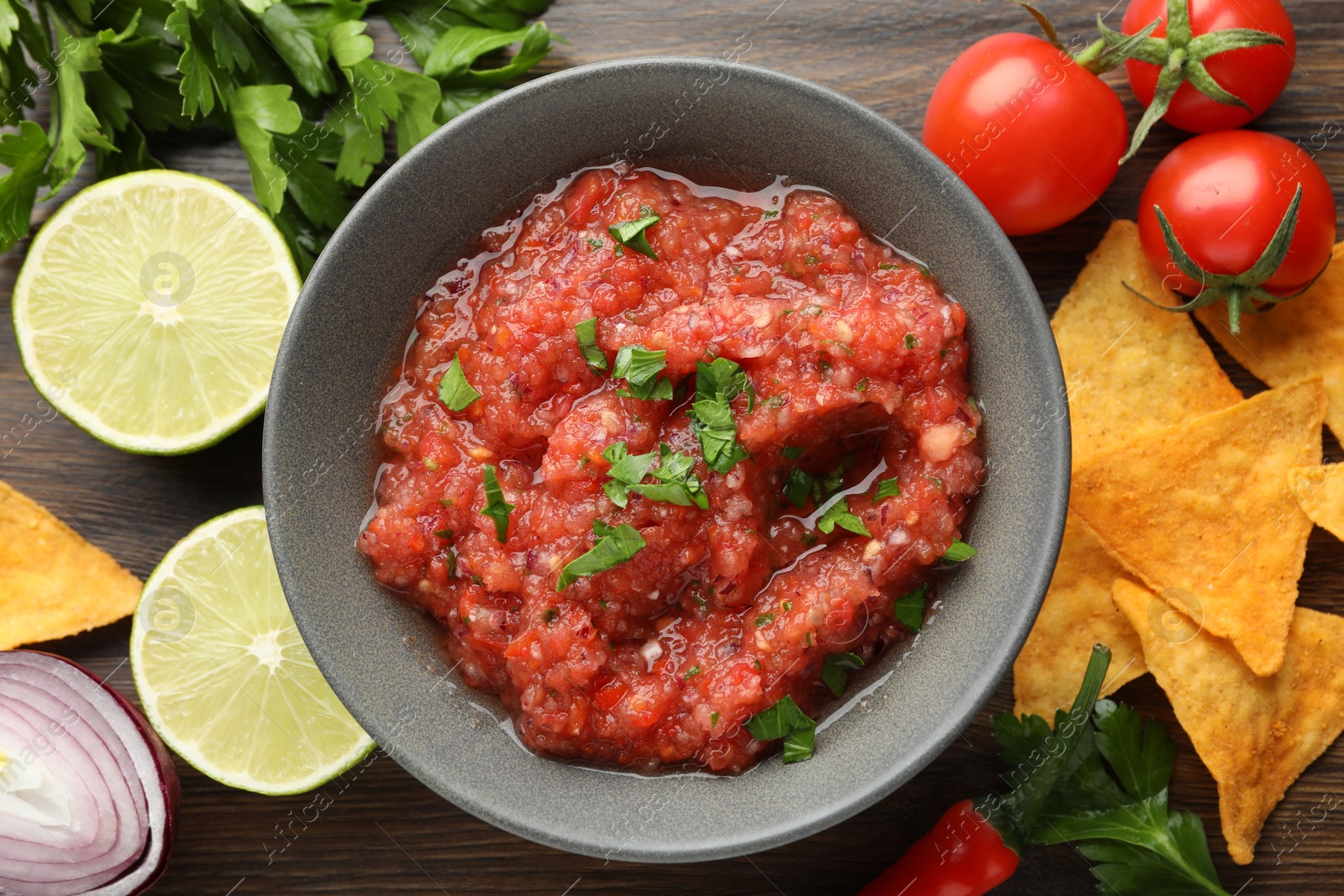 Photo of Delicious spicy salsa sauce in bowl and products on wooden table, flat lay