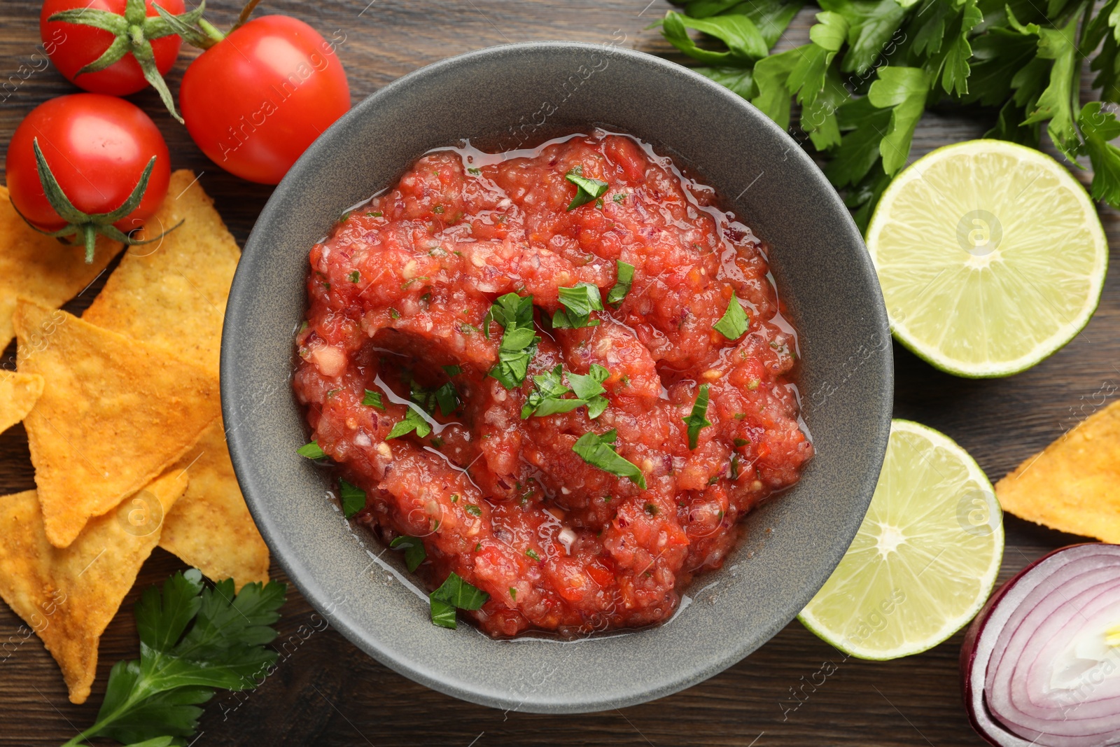 Photo of Delicious spicy salsa sauce in bowl and products on wooden table, flat lay