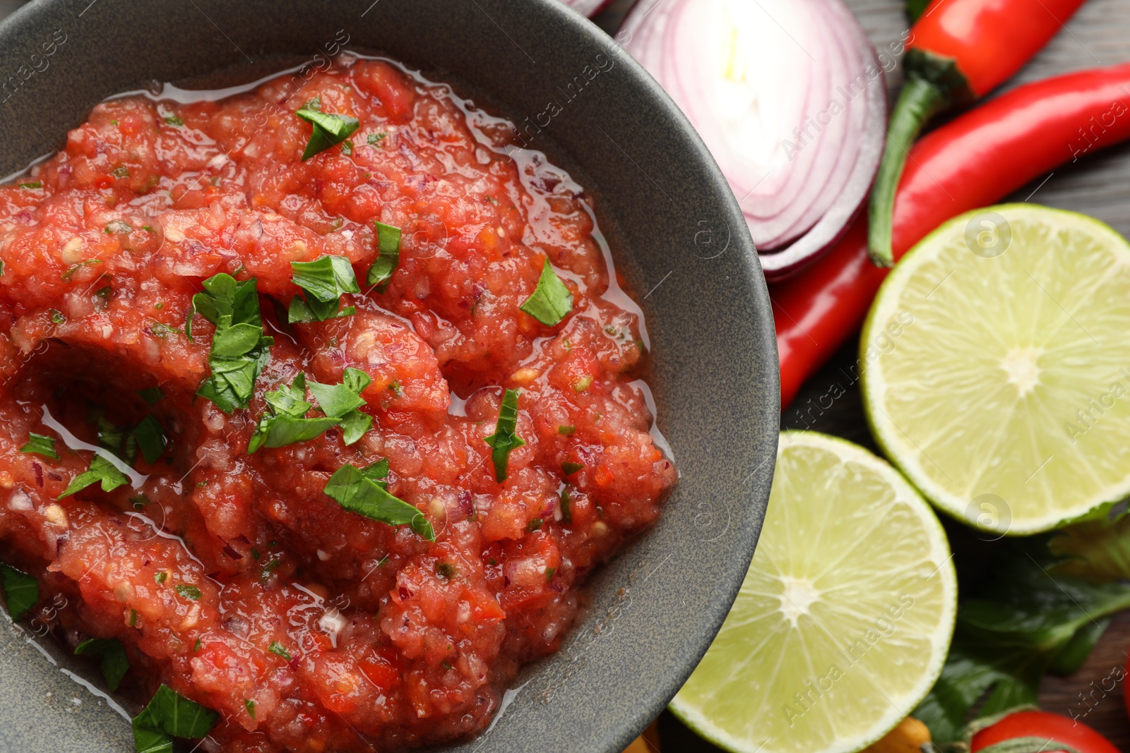 Photo of Delicious spicy salsa sauce in bowl and products on table, flat lay