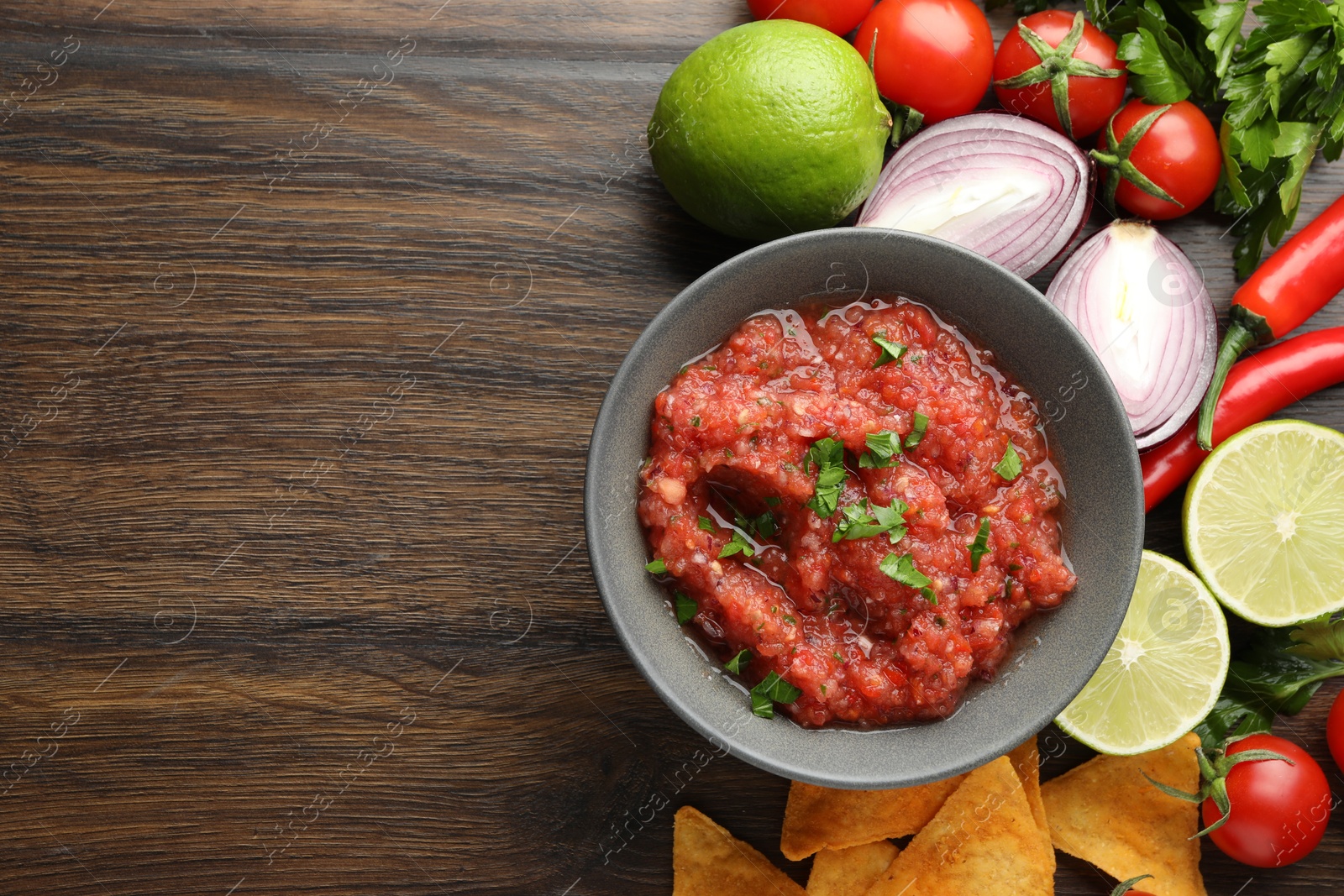 Photo of Delicious spicy salsa sauce in bowl and products on wooden table, flat lay. Space for text