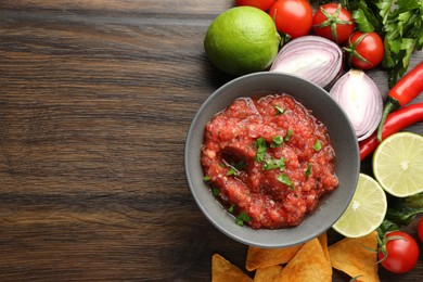 Delicious spicy salsa sauce in bowl and products on wooden table, flat lay. Space for text