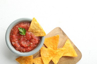 Delicious spicy salsa sauce in bowl and nacho chips on white table, flat lay