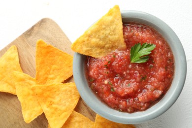 Delicious spicy salsa sauce in bowl and nacho chips on white table, flat lay