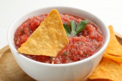 Photo of Delicious spicy salsa sauce with nacho chip in bowl on white table, closeup