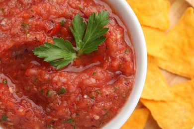 Delicious spicy salsa sauce in bowl and nacho chips on table, top view