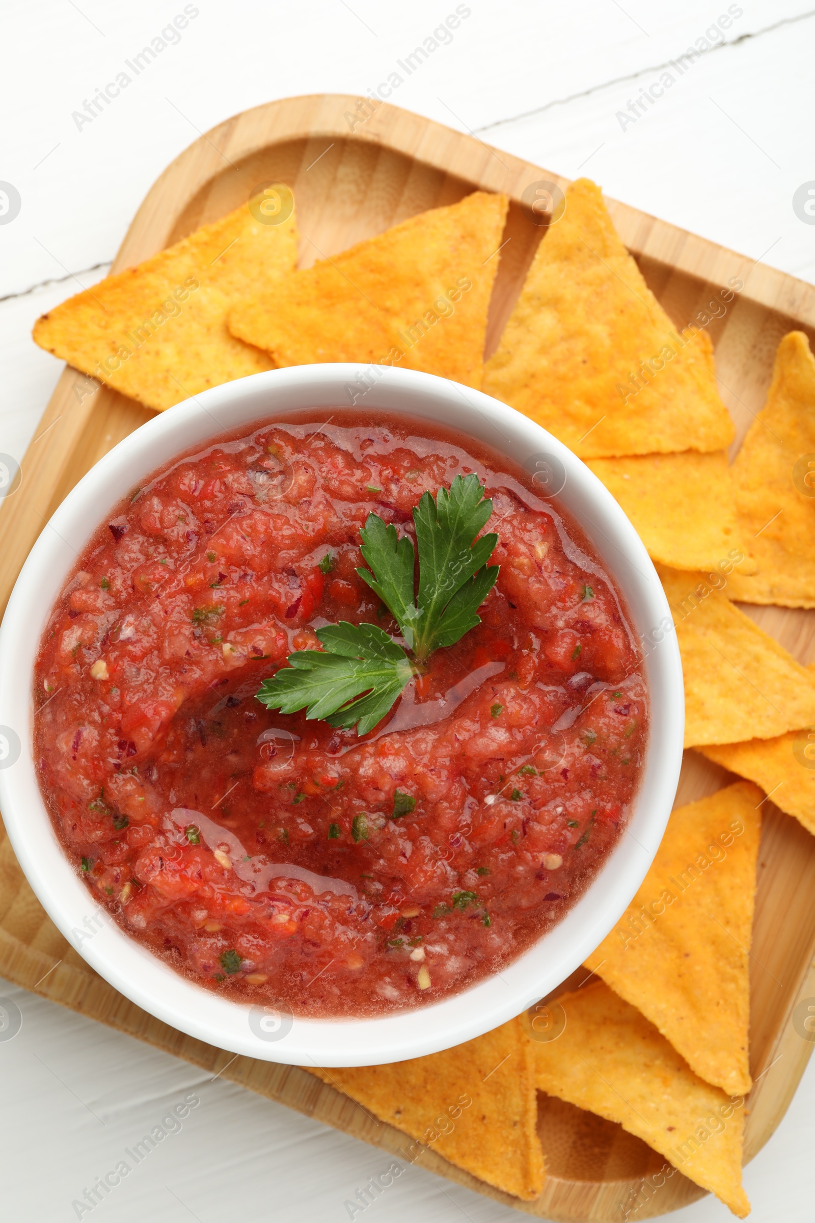 Photo of Delicious spicy salsa sauce in bowl and nacho chips on white wooden table, top view