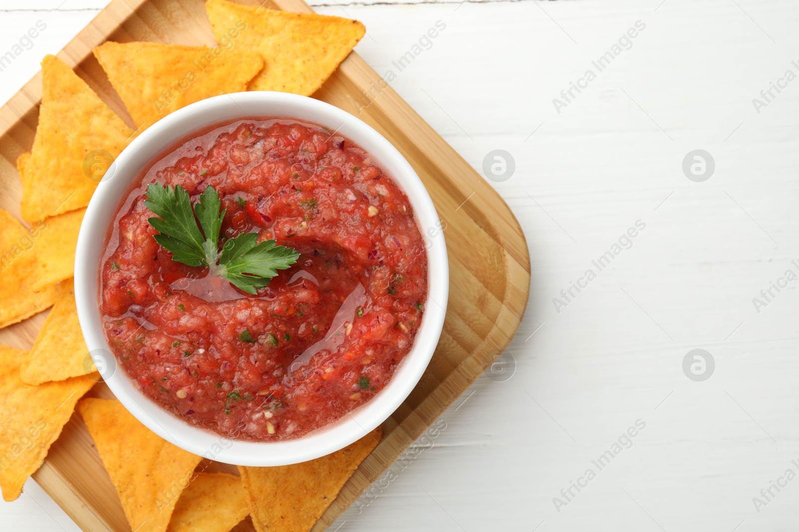 Photo of Delicious spicy salsa sauce in bowl and nacho chips on white wooden table, top view. Space for text