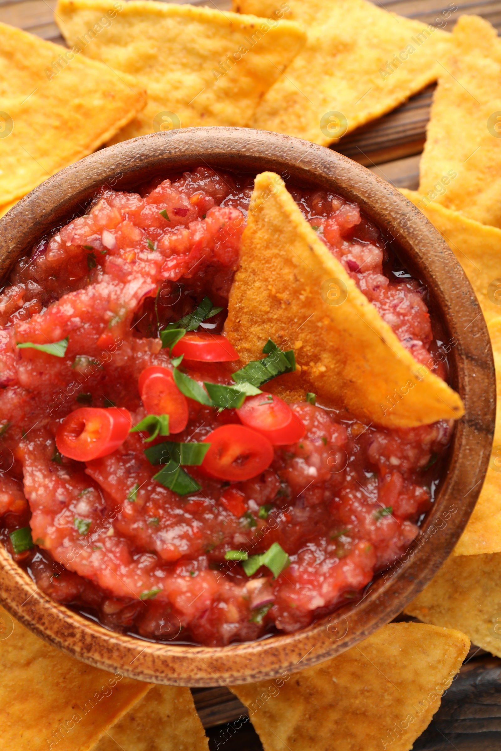 Photo of Delicious spicy salsa sauce in bowl and nacho chips on wooden table, top view