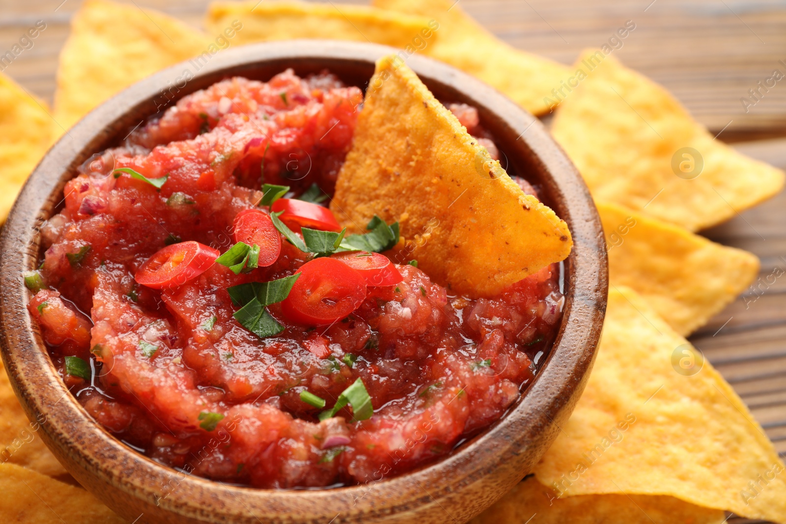 Photo of Delicious spicy salsa sauce in bowl and nacho chips on wooden table, closeup