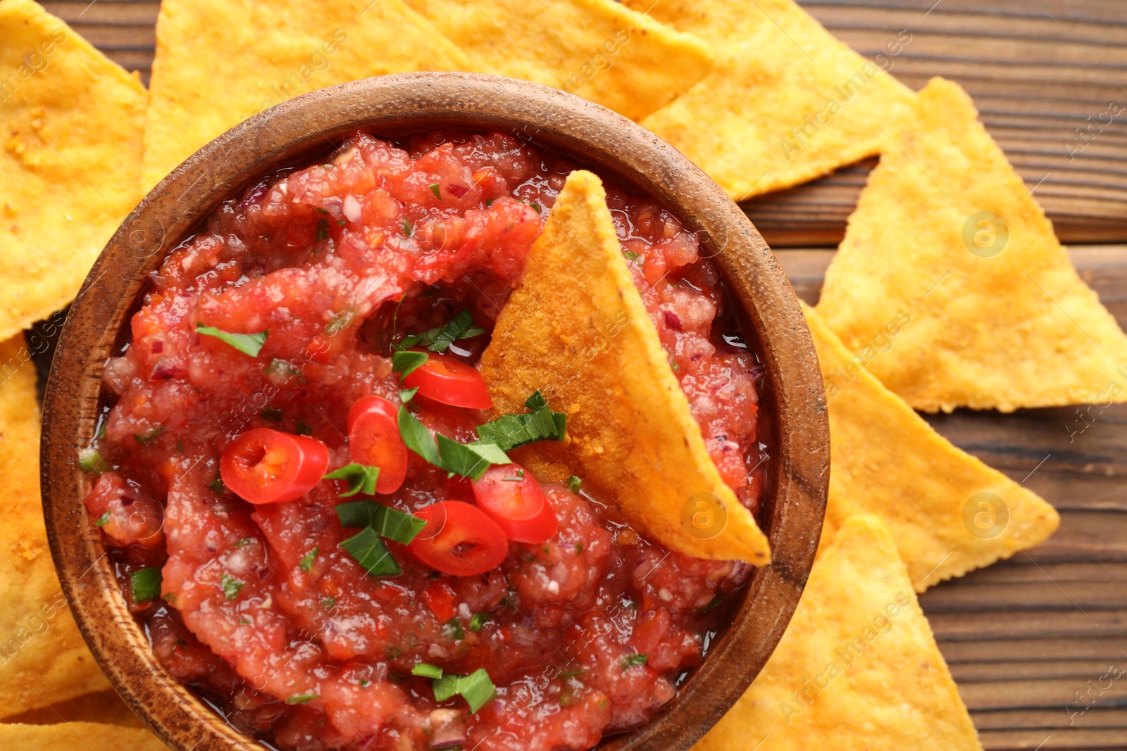 Photo of Delicious spicy salsa sauce in bowl and nacho chips on wooden table, flat lay